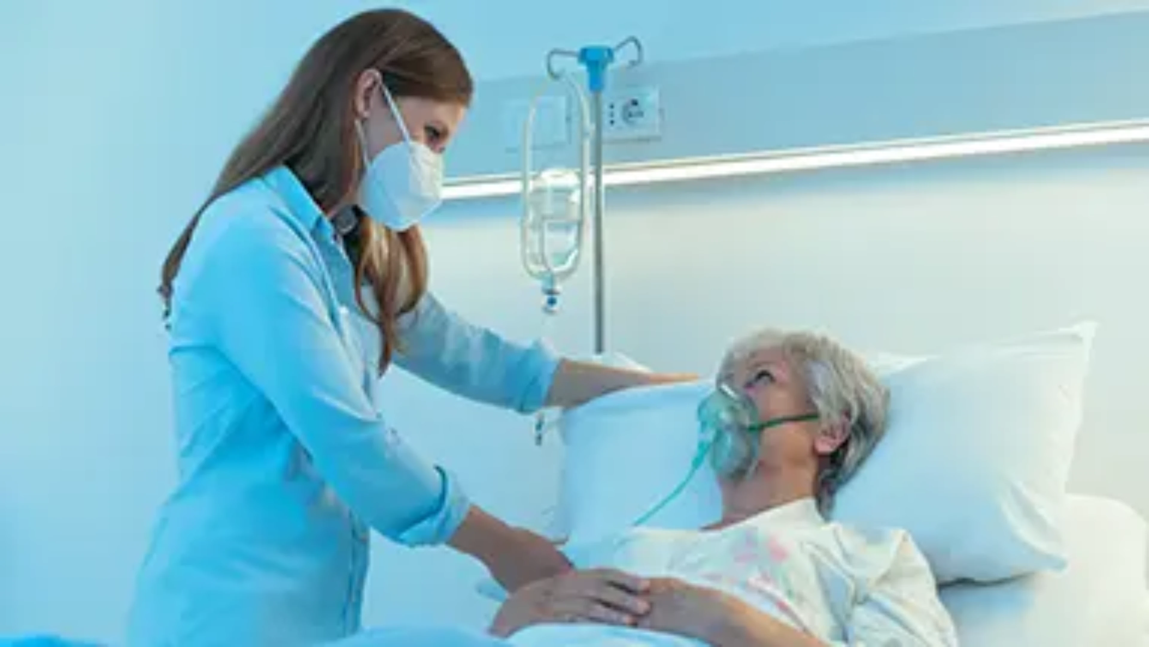 A nurse taking care of an elderly person in an hospital bed. The 2 people wear a surgical mask.