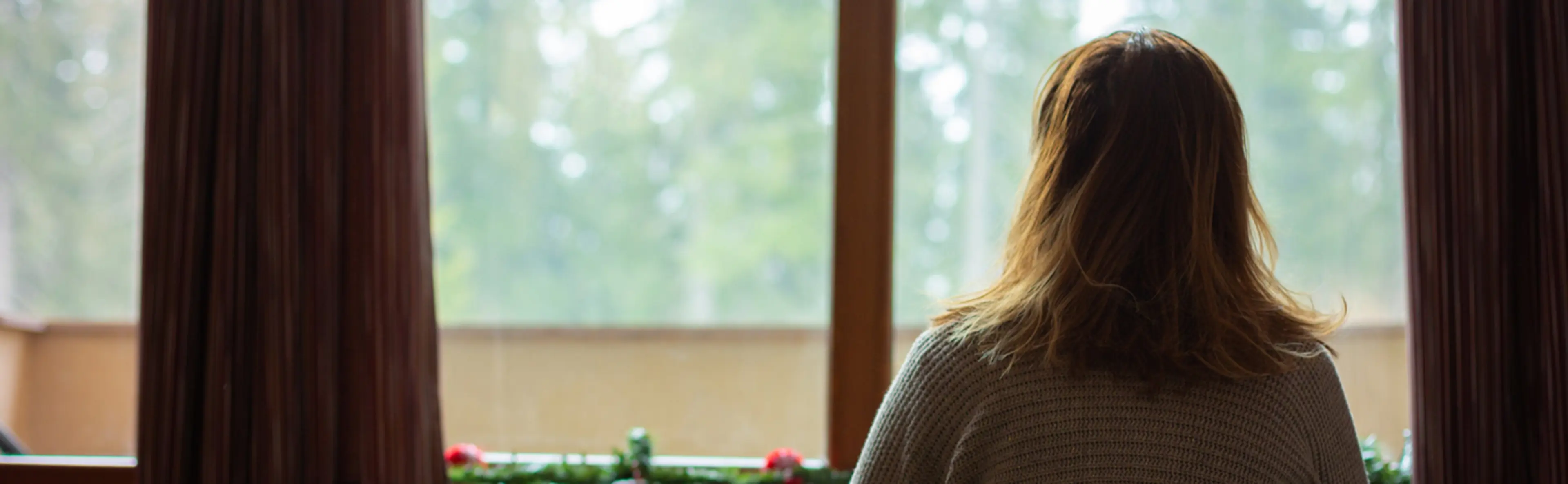 Femme regardant par la fenêtre un paysage enneigé, évoquant l'isolement lié à la dermatite atopique.