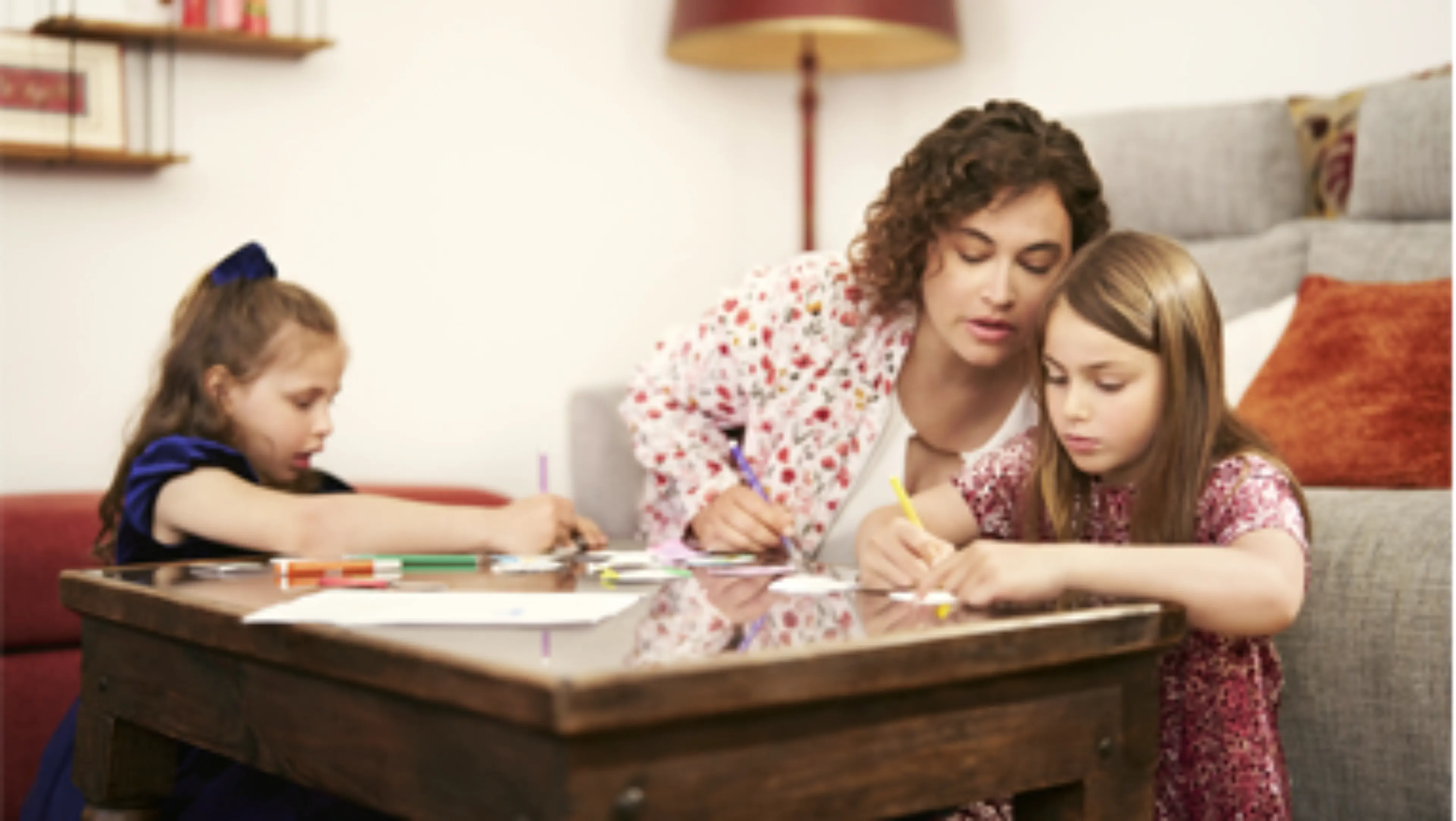 Une femme et deux petites filles sont assises ensemble autour d'une table, dessinant avec des crayons de couleur.