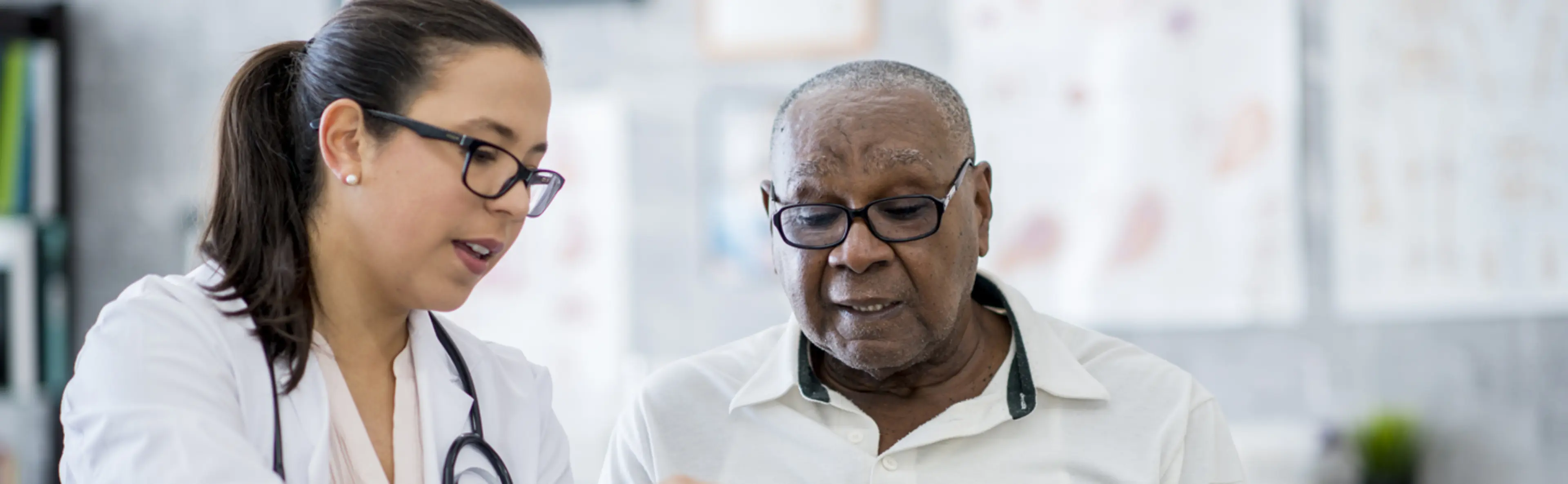 Professionnelle de santé en blouse blanche montrant une tablette à un patient âgé dans un cabinet médical.