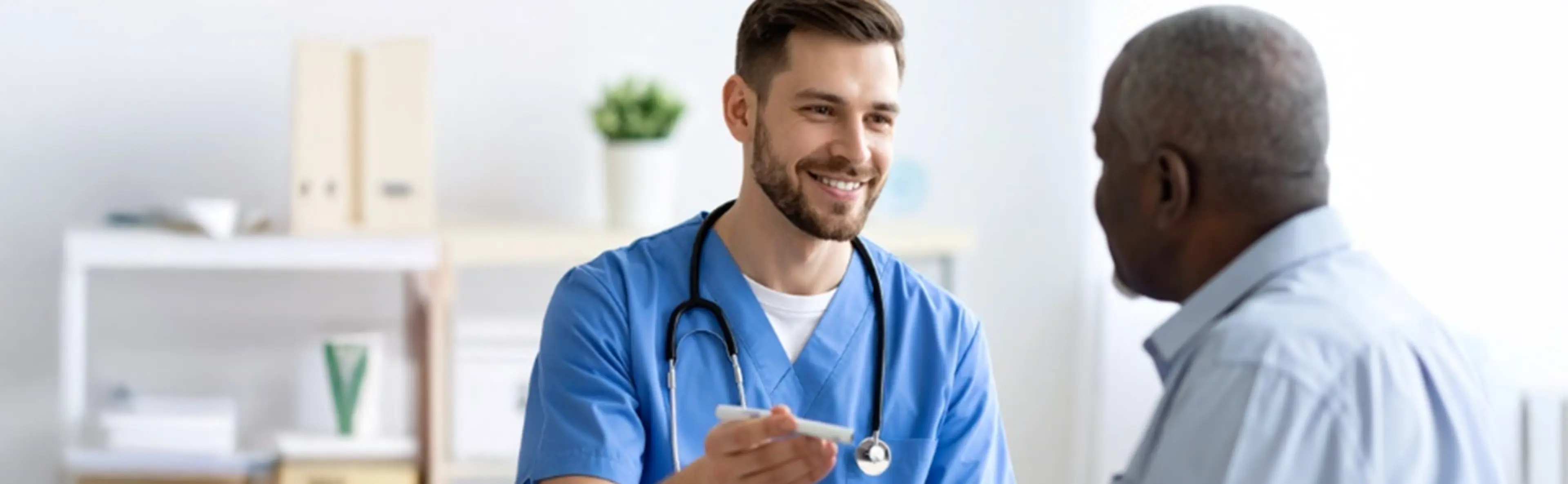 Médecin en blouse bleue souriant face à un patient dans un cabinet médical.
