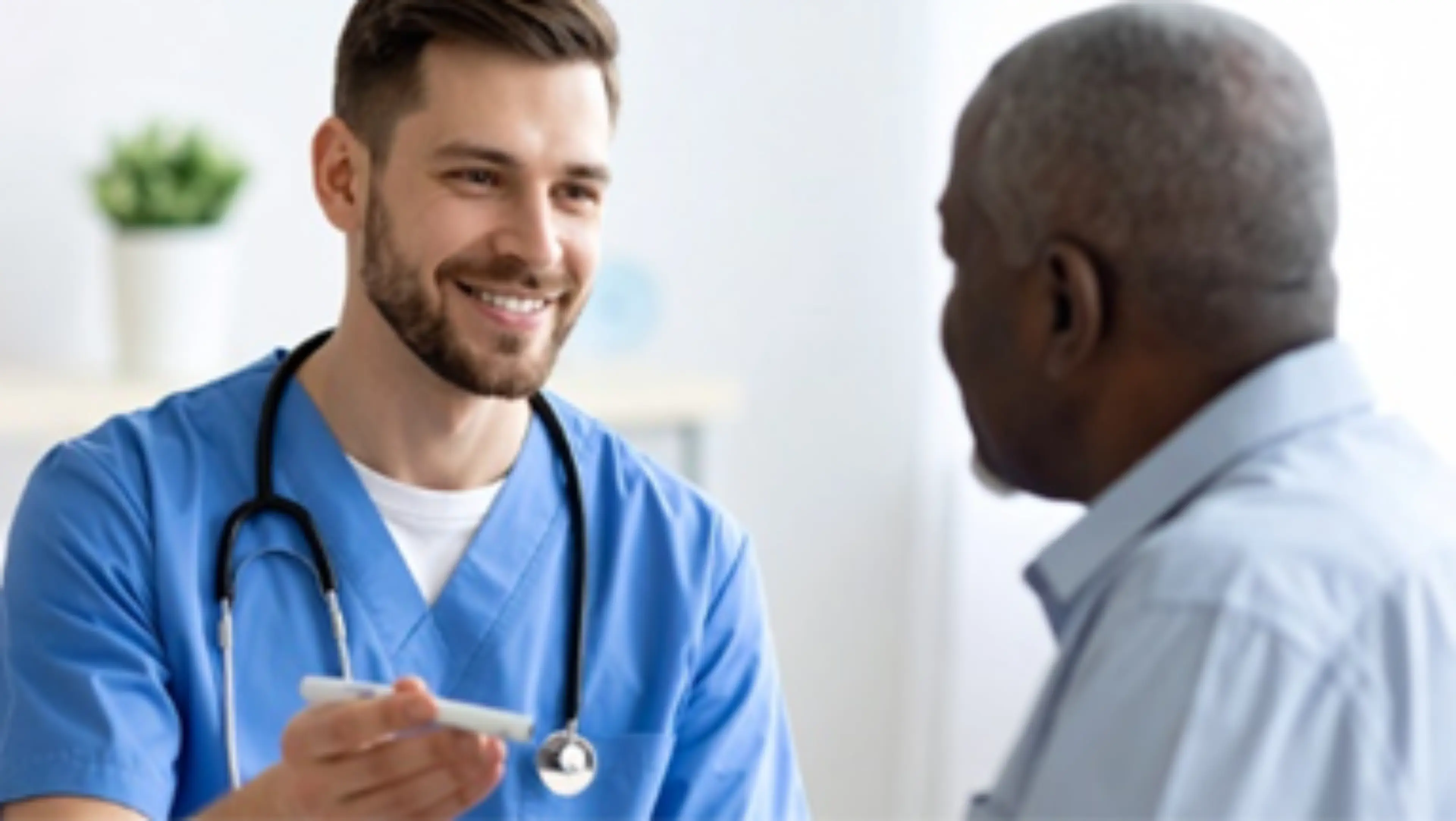 Médecin en blouse bleue souriant face à un patient dans un cabinet médical.