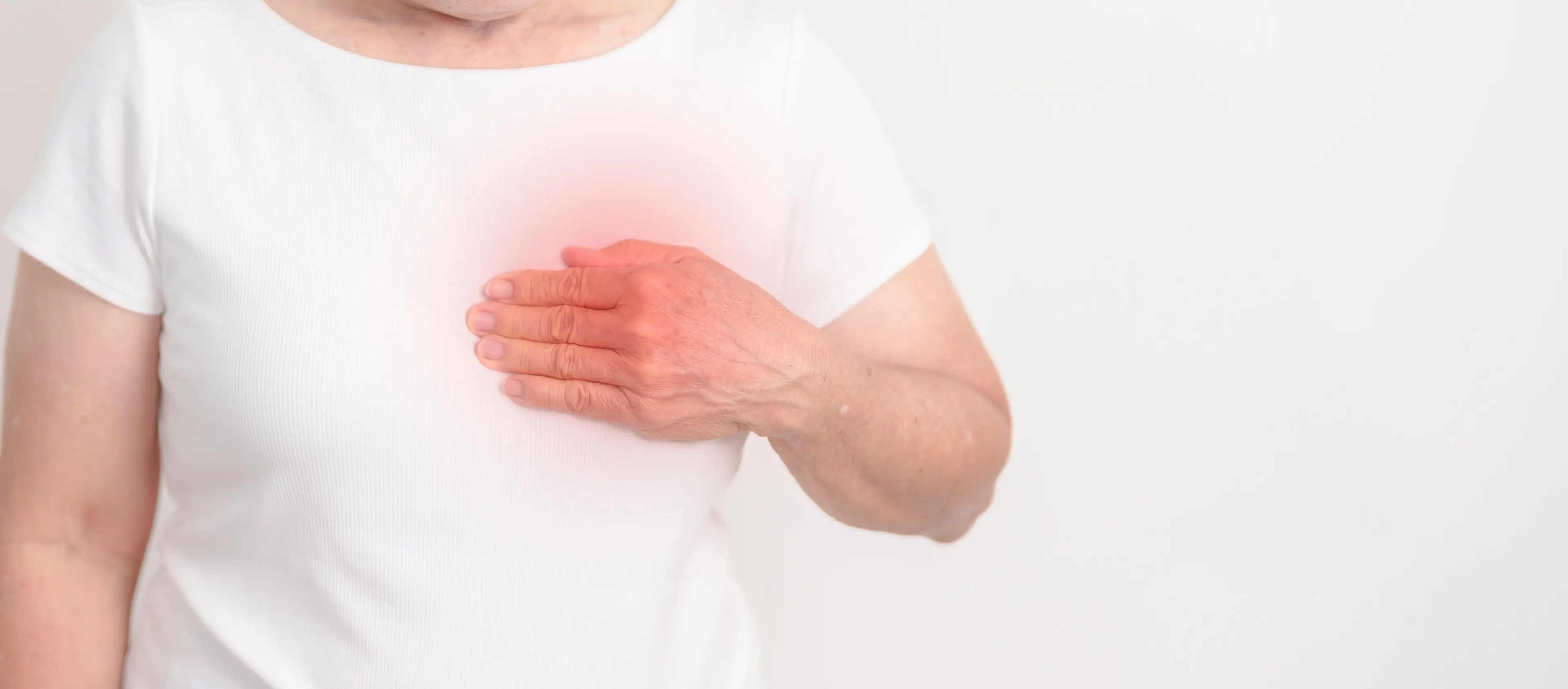 Oberkörper einer Person in weißem T-Shirt, die mit der rechten Hand die linke Brust berührt, Bereich der Brust gerötet