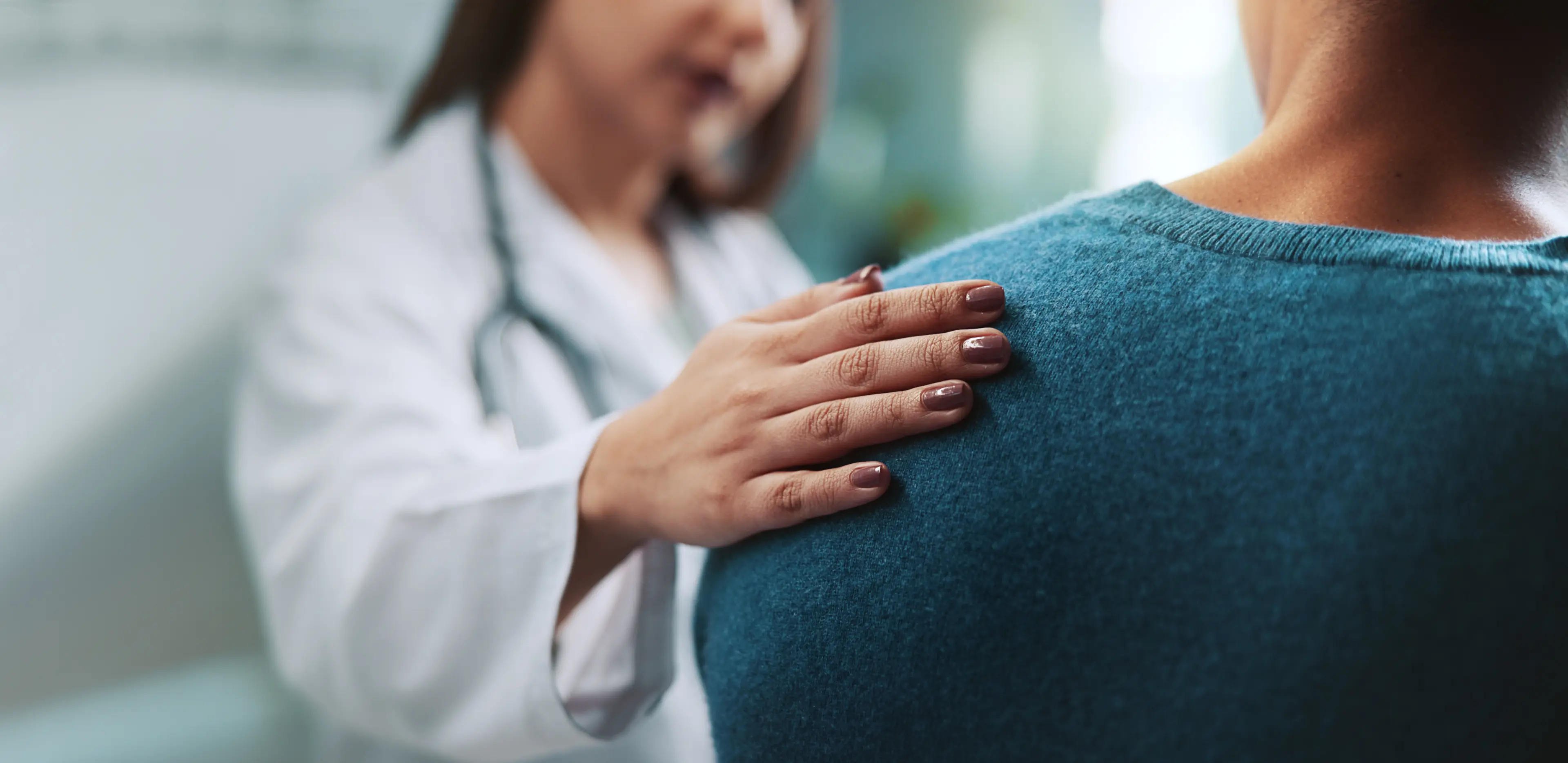 Ärztin legt beruhigend ihre Hand auf die Schulter eines sitzenden Patienten