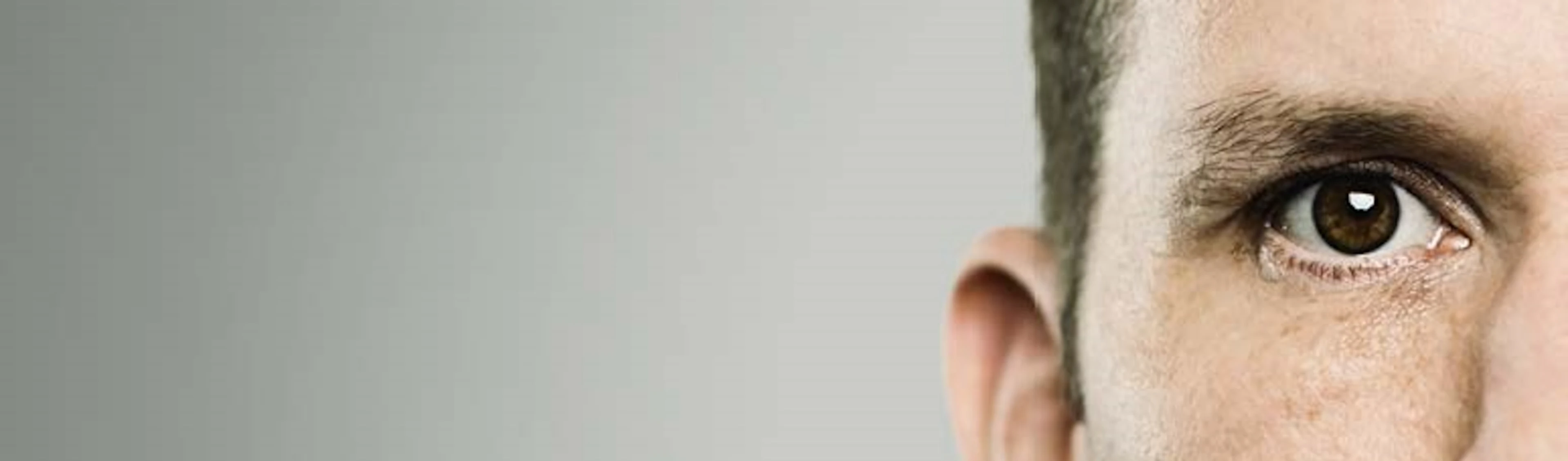 Nahaufnahme eines männlichen Gesichts mit braunem Auge und kurzem Haar, nur rechte Gesichtshälfte sichtbar.