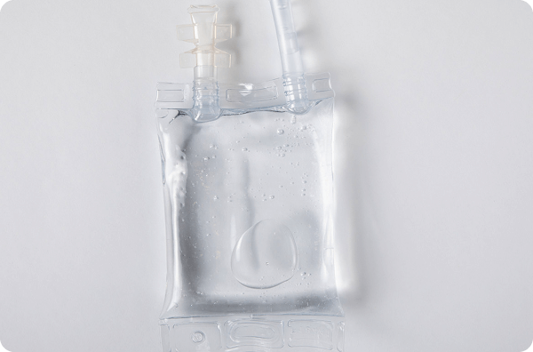 Image of clear intravenous infusion bag filled with fluid, with connected tubing and ports, set against a plain white background.
