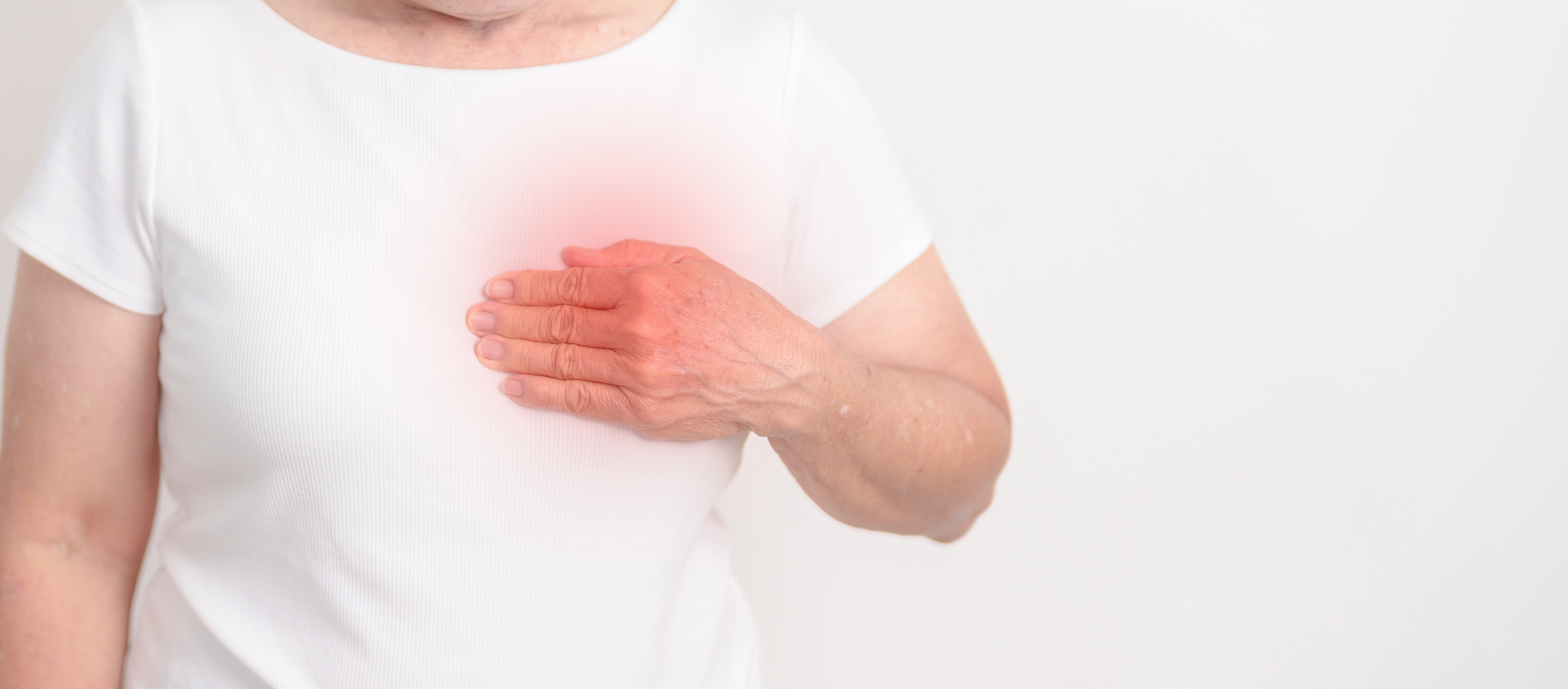 Oberkörper einer Person in weißem T-Shirt, die mit der rechten Hand die linke Brust berührt, Bereich der Brust gerötet