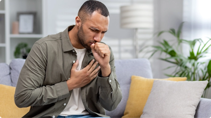An adult coughing while sitting on a couch