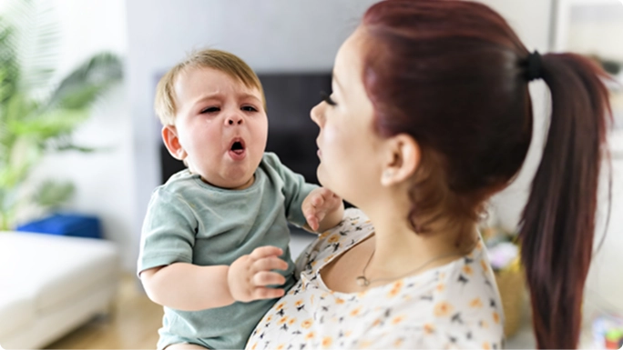 A baby coughing while resting on his mother’s arm