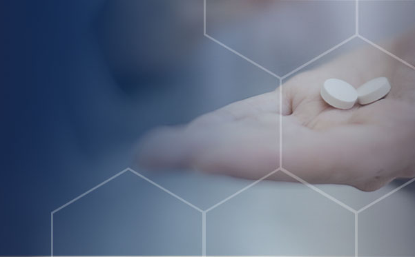 Close-up of a hand holding two white pills with a blue background and a white outlined hexagonal pattern fading into a white gradient.